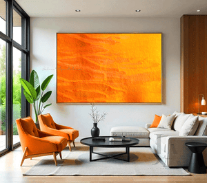 A large orange minimalist painting , displayed on white wall in a modern living room with a white sofa, two orange armchairs , a black low coffee table and a large window overlooking a natural landscape , creating a warm and inviting atmosphere