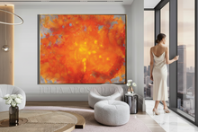 Modern living room with oversize orange abstract art, gray sofa, and woman looking out a window city view.
