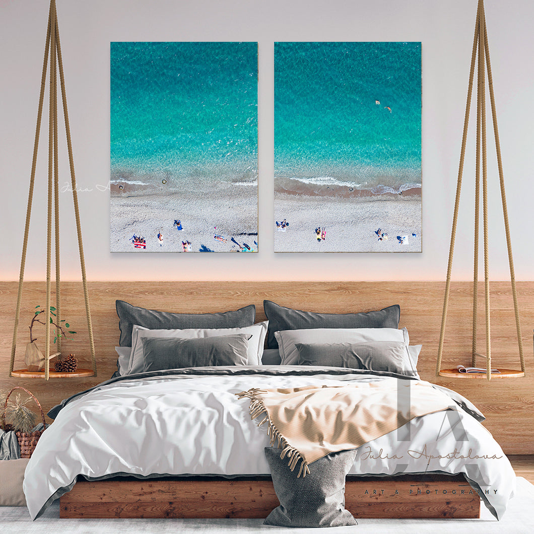 A large coastal-inspired minimalist beach wall art set on the wall, futured people on the beach, turquoise waters, and ocean waves. The set is hanging over bed, in boho bedroom decor setting. The room futures white walls, a  bed surrounded with pillows, plans, a low wooden coffee table and a decorative boho accents.