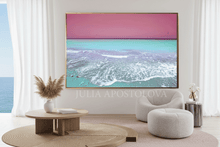 Modern living room with a large turquoise ocean wall art with pink sky, surrounded by minimal decor, and an ocean view.