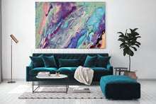 A large square abstract canvas print with swirling purple, teal, pink, and cream marbled patterns, displayed on a white wall above a dark teal velvet sofa in a modern living room setting.