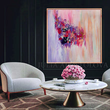 A large square abstract canvas painting with pink, purple, red, and peach brushstrokes hangs on a dark paneled wall above a marble coffee table with pink roses in a bowl, flanked by two light gray armchairs.