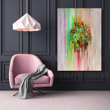 A colorful abstract canvas painting by artist Julia Apostolova, with green, red, pink, and yellow brushstrokes, displayed on a dark paneled wall above a pink armchair in a modern room setting.
