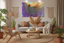 A large abstract canvas wall art print with a colorful fluid art pattern in purple, gold, teal, and gray, displayed above a modern gray sofa in a styled living room setting.