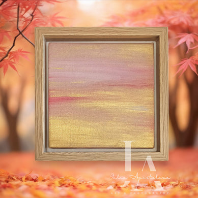 A wooden frame with a painted landscape inside, featuring a sunset golden sky pale rose pink hues. The frame is surrounded by blurred autumn leaves in shades of pink, orange, and yellow, creating a cozy and serene atmosphere.