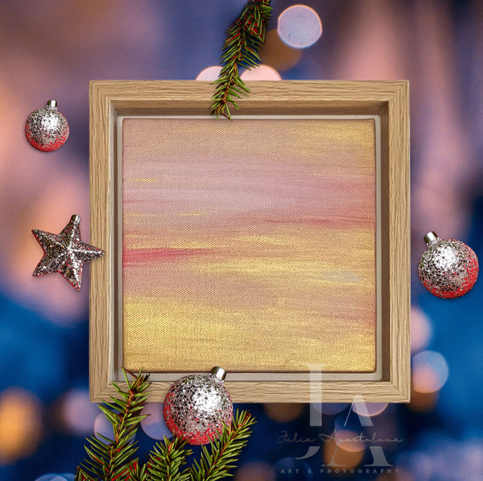 A wooden framed original painting depicting a serene abstract minimalist landscape with gold and pale pink color scheme. The frame is surrounded by Christmas decorations such as pine branches, Christmas balls, and lights in the background 