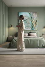 Woman in a white outfit standing in a bedroom with a large sage abstract painting on the wall, painted by artist Julia Apostolova