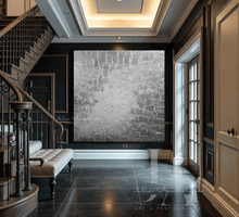 A large silver gray abstract minimalist painting featuring bold brushstrokes of gray, and silver colors on a canvas displayed in a grand entryway with hardwood floors , a chandelier , and wooden staircase