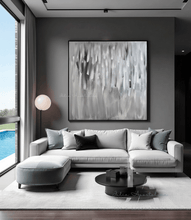 Modern living room with a gray sectional sofa, silver abstract painting, and round coffee table.