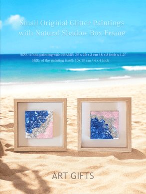 Two wooden frames with a small original glitter paintings inside, featuring an abstract seascapes with blue sea , silver glitter waves , and pale rose pink sand. Two original artworks, unique abstract glitter seascape paintings, one-of-a-kind wall art , perfect gift for her, and for coastal decor. The paintings are surrounded by blurred coastal background with blue ocean, sandy beach , creating a cozy and serene atmosphere. 
