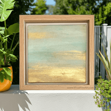 Framed abstract artwork with gold and green hues on a table outdoors.
