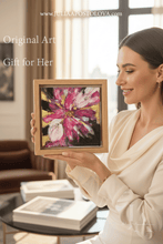 Woman holding a framed abstract painting with pink and white flowers and golden details. Home setting
