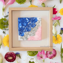Framed abstract art piece with blue, silver, and pink colors on a floral background.