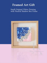 A wooden frame with a small glitter painting inside, featuring an abstract seascape with blue sea , silver glitter waves , and pale rose pink sand. The frame is surrounded by blurred background in shades of blue , pastel pink, creating a cozy and serene atmosphere. Original artwork, unique abstract glitter seascape painting, one-of-a-kind wall art , perfect gift for her, and for coastal decor.