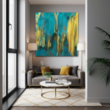 Modern living room with teal gold abstract art, above gray sofa with yellow / gold pillows, a round coffee table with gold accents, a plant, and a large window.