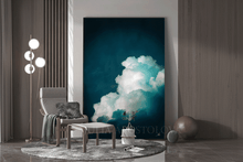 Oversized vertical canvas painting print by artist Julia Apostolova, featuring a dramatic teal and white cloud scene, displayed in a modern living room setting next to a gray armchair, floor lamp, and decorative spheres.
