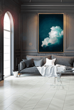 A large framed wall art print depicting white clouds against a deep teal and black sky, displayed in a gold frame on a dark paneled wall above a gray sofa in a modern living room setting.