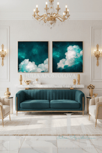 A modern living room featuring a teal velvet sofa with gold trim, flanked by beige armchairs, a white marble console, and two matching framed teal cloud paintings on the wall. A large gold chandelier hangs above.