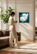 A woman in a cream satin jumpsuit stands in a bright living room next to a sofa, looking at a framed square art print depicting white clouds in a deep  teal sky. The image has text overlays at the top and bottom.