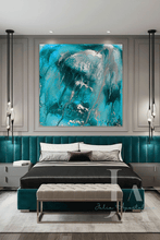 A large square abstract wall art print with swirling turquoise, teal, and silver brushstrokes, displayed above a modern bed in a styled bedroom setting.