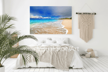 Beach scene wall art above a bed in a bedroom with a plant and macrame hanging.