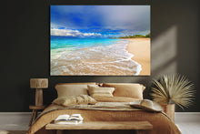 Beach scene painting on a wall above a bed with pillows and an open book.