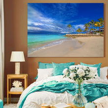 Beach scene painting above a bed with teal and white bedding.