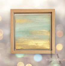 A serene minimalist landscape painting with metallic gold and pastel turquoise color scheme. The abstract sky is filled with warm hues of gold, reflecting on the calm, pale turquoise abstract waters below. The painting is framed in a simple, wooden frame. Will be perfect elegant gift for someone special.