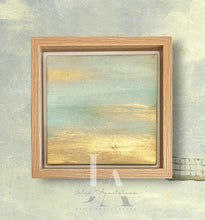 A framed painting depicting a serene landscape with a sunset sky. The painting shows a tranquil scene with a warm, golden horizon and soft, pastel colors in the sky. The frame is made of light-colored wood, adding to the natural, calming feel of the artwork