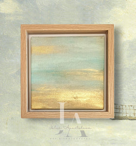 A framed painting depicting a serene landscape with a sunset sky. The painting shows a tranquil scene with a warm, golden horizon and soft, pastel colors in the sky. The frame is made of light-colored wood, adding to the natural, calming feel of the artwork