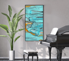 A vertical framed abstract wall art by artist Julia Apostolova with swirling turquoise, teal, blue, gray, and gold paint patterns, displayed on a light gray wall in a styled room next to a green potted plant and a black grand piano.