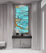 Abstract wall art by artist Julia Apostolova featuring swirling turquoise, teal, gray, black, and gold marbled patterns, displayed in a tall vertical frame on a gray paneled wall above a console table.