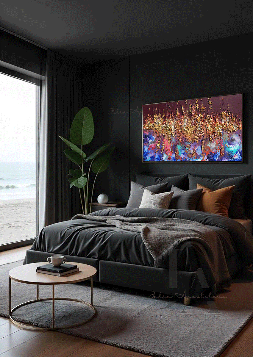 A modern dark bedroom, featuring a dark-grey, velvet bed, a low, round coffee table made of wood and gold metal, and a large colorful abstract painting with gold and copper rich 3d textures on the wall. The room overlooks a coastline through floor-to-ceiling windows. The setting sun casts a warm, natural glow across the scene.