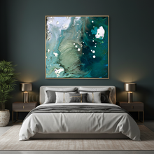A square abstract wall art print with swirling teal, aqua, white, and gray marbled patterns, framed in a thin gold border, hanging above a neatly made bed in a modern bedroom setting.