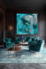 A large abstract painting in vibrant turquoise, teal, and silver tones hangs on a dark wood-paneled wall above a matching teal velvet sofa, two matching armchairs, and a patterned blue-green rug in a luxury living room setting.
