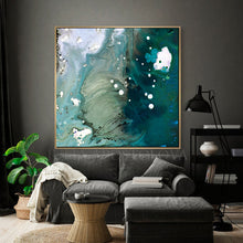A large framed abstract canvas print with swirling teal, aqua, white, and gray paint, hanging on a dark gray wall above a modern gray sofa in a styled living room.