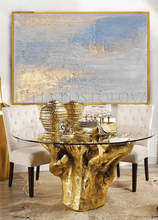 Gold leaf dining table with glass top in a room with abstract art on the wall.