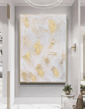 Abstract gold and white painting on a wall in a modern interior setting.