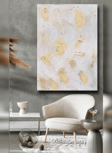 Abstract art piece with gold accents on a gray wall above a modern chair.