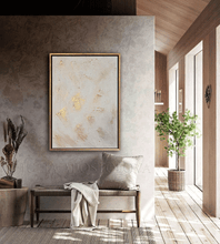Modern living room with white gold abstract art, hanging over bench. There are plants and a large windows with natural light