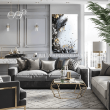 Modern living room with black white gold leaf painting, gray sectional sofa, decorative pillows, and a geometric coffee table with glass and gold accents.