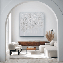 Modern living room with white walls, a large wabi sabi white 3d textured abstract painting by artist Julia Apostolova, and minimal furniture.