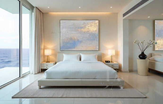 Modern bedroom with large minimalist painting over the bed, a windows with ocean view, bed, lights and decorative elements.