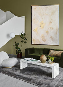 Modern living room with green sofa, white armchair, and abstract art on olive green wall.