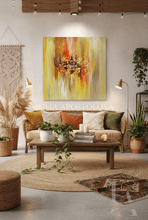 An abstract oil painting by Julia Apostolova featuring vibrant yellow, orange, and red brushstrokes, displayed on a beige wall in a modern, cozy living room setting with a wooden sofa, coffee table, and potted plants.