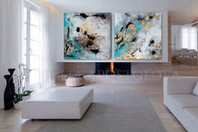 Two abstract gold leaf paintings with black, gold leaf, gray, and teal colors displayed in a modern interior setting with a fireplace and white furniture.