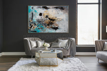A gray velvet sofa with a mirrored coffee table and a large abstract painting with black, white, gold leaf, and teal colors. The painting is titled ''Calm After The storm'', painted by artist Julia Apostolova.