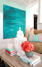 A canvas gallery wrap print featuring an abstract coastal art piece in turquoise, teal, and white displayed in a living room setting. The artwork is signed by artist Julia Apostolova and is ready to hang.